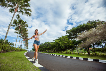 Sexy fashionable girl in a swimsuit and shorts in big sneakers walks on the curb on the background of palm trees, friends balance.