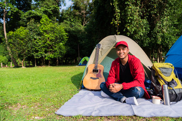 Young asian tourist backpacker sitting in a tent camping in Forest. Image of camping,travel,lifestyle or recreation concept.