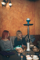 Two girls relax, have fun in the cafe. smoke hookah drink tea. The concept of smoking tobacco, refueling mix for hookah. Vertical photo