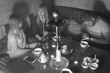 Smoke hookah shisha in bar and nightclub, team of friends two girls and man, have fun, drink tea. Black and white, bw