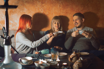 Smoke hookah shisha in bar and nightclub, team of friends two girls and man, have fun, drink tea.