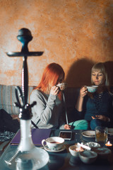 Two girls relax, have fun in the cafe. smoke hookah drink tea. The concept of smoking tobacco, refueling mix for hookah. Vertical photo