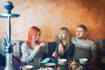 Smoke hookah shisha in bar and nightclub, team of friends two girls and man, have fun, drink tea. something in the cup, beetle in the cup, unsanitary conditions