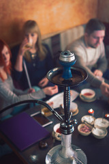 Smoke hookah shisha in bar and nightclub, team of friends two girls and man, have fun, drink tea.