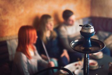 Smoke hookah shisha in bar and nightclub, team of friends two girls and man, have fun, drink tea.