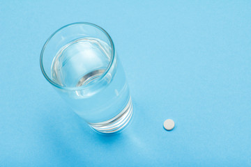 Glass of water and pill on blue background.