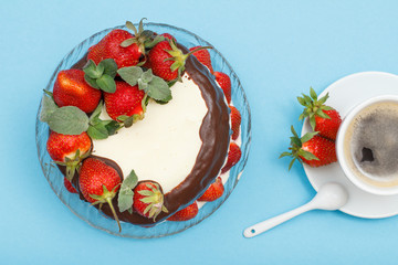 Homemade chocolate cake decorated with fresh strawberries on glass plate and cup of coffee with saucer.