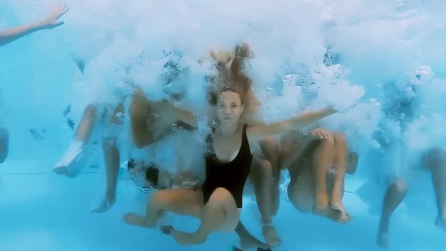 Underwater view of happy fun loving group of friends jumping and diving into swimming pool at a pool party in summer sunny day. Slow motion.