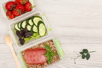 Plastic meal prep containers with boiled buckwheat porridge and slices of meat, fresh vegetables and berries.