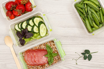 Plastic meal prep containers with boiled buckwheat porridge and slices of meat, fresh vegetables and berries.