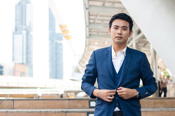 Confident businessman, Young businessman in blue suit fasten the bottons standing outdoor in the city.