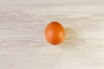 One brown chicken egg in the center of a beige wooden table, top view.