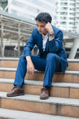 Sad yound and handsome businessman sit on the stair and have bad feeling.