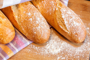 Three fresh crunchy baguettes in flour on a wooden board covered with a striped towel close-up.