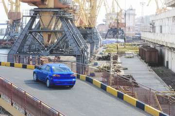 Naklejka premium Blue passenger car in the seaport on the background of cranes after unloading. Freight transportation, shipment and delivery import export concept.