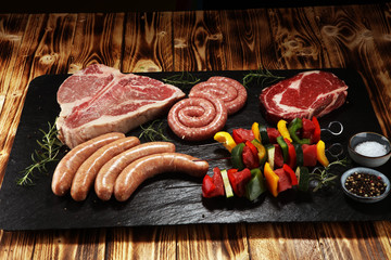 Assorted delicious raw meat with vegetable on a barbecue with t-bone steak, sausages and meat...