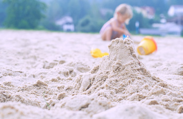 Little blonde baby girl playing with sand on the beach using plastic toys.