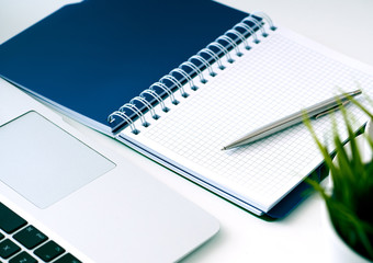 Closeup of white desktop with laptop, coffee cup, notepads, pen, calculator and other items.
