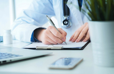 Female doctor filling up prescription form or patient history list at clipboard pad during physical...
