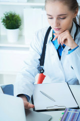 Female doctor working on medical expertise while sitting at desk in front of laptop. Young therapist looks seriously at the laptop screen.