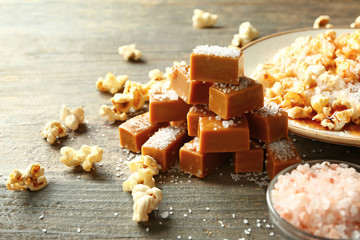 Tasty salty caramel candies with popcorn on wooden table