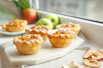 Board with tasty apple pies on windowsill