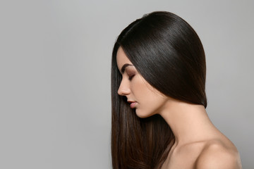 Portrait of beautiful young woman with healthy long hair on grey background