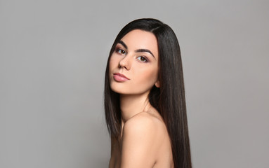 Portrait of beautiful young woman with healthy long hair on grey background