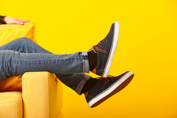 Stylish man in shoes sitting in armchair on color background - obrazy, fototapety, plakaty