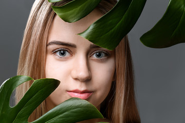 Beautiful young woman with laminated eyelashes and tropical leaves on grey background