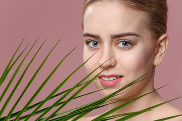 Beautiful young woman with laminated eyelashes and tropical leaf on color background