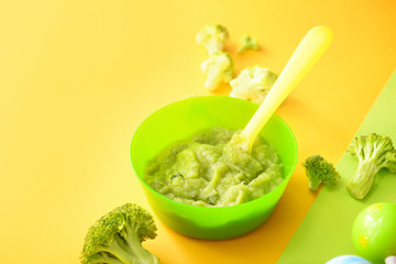 Bowl with healthy baby food on color background