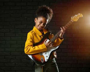 African-American girl playing guitar against dark wall