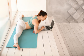 Sporty young woman with laptop doing leg-split in gym
