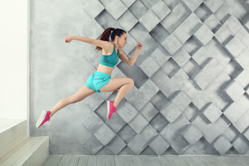 Sporty running woman against grey wall