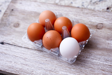 Set of brown and white eggs in clear plastic box on wooden table.