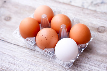 Set of brown and white eggs in clear plastic box on wooden table.