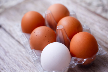 Set of brown and white eggs in clear plastic box on wooden table.