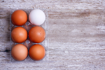 Set of brown and white eggs in clear plastic box on wooden table.
