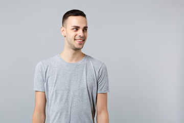 Portrait of smiling attractive young man in casual clothes standing and looking aside isolated on grey wall background in studio. People sincere emotions, lifestyle concept. Mock up copy space.