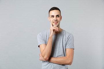 Portrait of pensive young man in casual clothes looking aside and put hand prop up on chin isolated on grey wall background in studio. People sincere emotions, lifestyle concept. Mock up copy space.