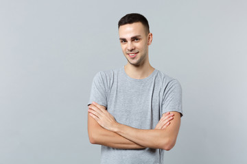 Portrait of smiling handsome young man in casual clothes looking camera, holding hands crossed isolated on grey background in studio. People sincere emotions, lifestyle concept. Mock up copy space.