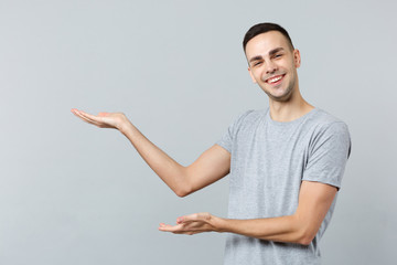 Portrait of cheerful funny young man in casual clothes looking camera, pointing hand aside isolated on grey wall background in studio. People sincere emotions, lifestyle concept. Mock up copy space.