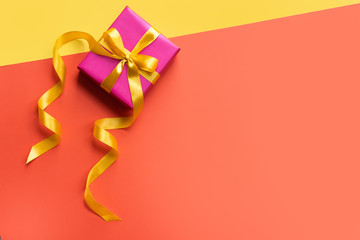 Present on color background. Gift box with yellow ribbon on orange desk. Copy spase