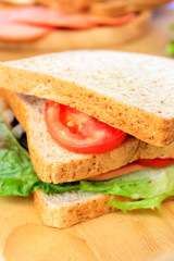 Homemade sandwich breakfast preparing. Close up whole wheat sandwich bread with slice tomatoes and lettuce stacked on wooden cutting board. Cooking ingredient. Food background concept.