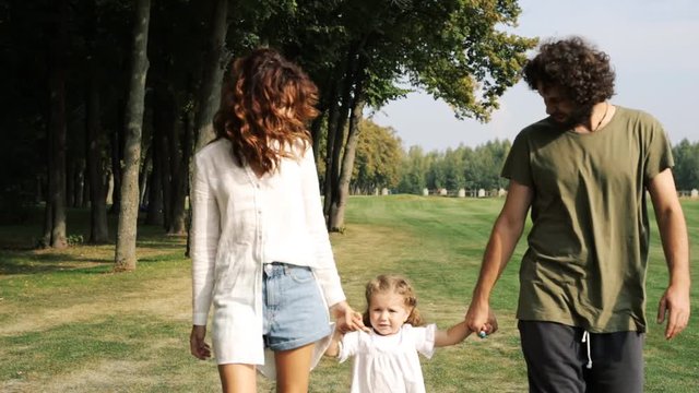 Family with a child walks on a green lawn in the park. Steadicam shot.