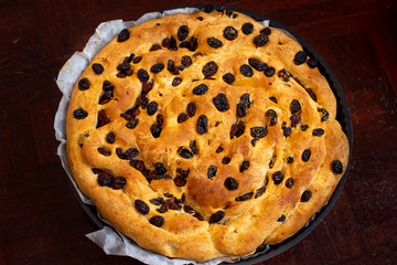 Cake made of bread with dried raisins in a round baking pan on a black background