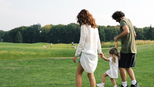 Family with a child walks on a green lawn in the park. Steadicam shot.