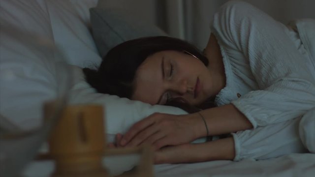Natural girl sleeping in bedroom indoors close up 4k video shot handheld camera. Brunette woman relaxing lying in bed with closed eyes. Healthy life habits self-care. Stress overcome dream relaxation