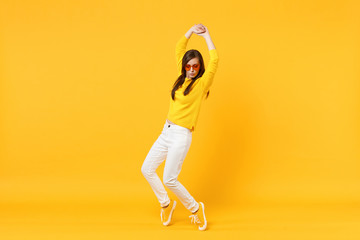 Fototapeta na wymiar Cute young woman in casual clothes, heart glasses looking down, rising hands, dancing isolated on yellow orange background in studio. People sincere emotions, lifestyle concept. Mock up copy space.